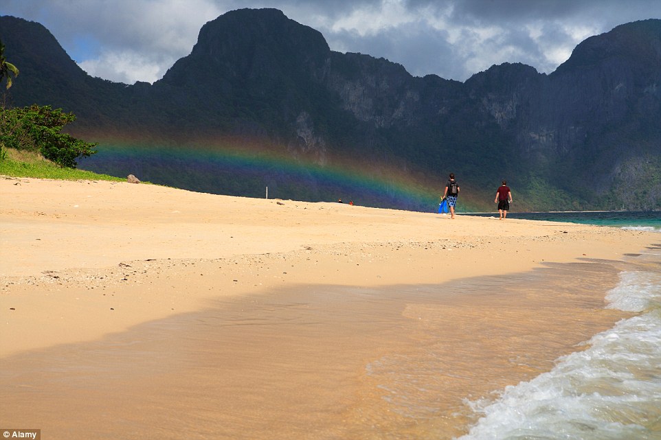 旅客漫步沙灘，有彩虹作為背景相當浪漫。(圖片來源／dailymail）