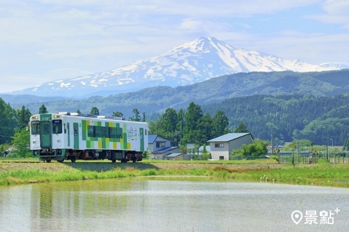 藍、綠、紅三色玩具列車中的綠色列車與鳥海山同框畫面。（圖 / 由利高原鐵道）